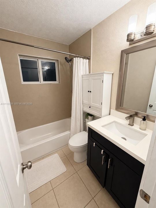 Bathroom featuring a dark-finish vanity with a white countertop and rectangular undermount sink, wall-mounted white cabinetry, tile flooring, and a shower-tub combination with tile surround