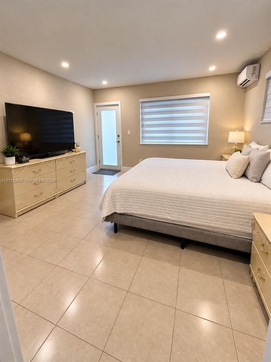Neutral-toned ceramic tile flooring, recessed ceiling lighting, wall-mounted climate control unit, and window with adjustable light-filtering shade