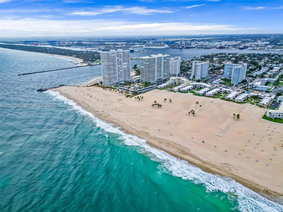 Aerial perspective of a high-rise residential complex located on a coastal shoreline featuring an expansive sandy beach and oceanfront access