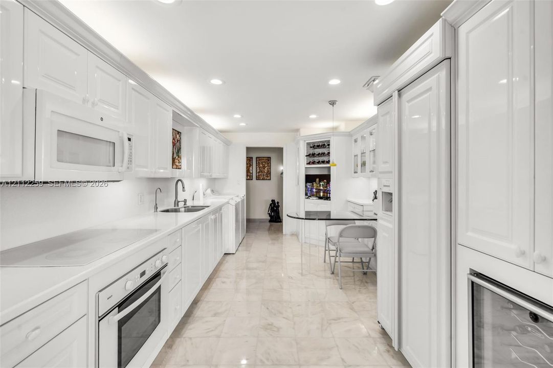 Kitchen featuring high-gloss white cabinetry, stone flooring, built-in panel-ready refrigerator, stainless steel oven, and integrated wine storage