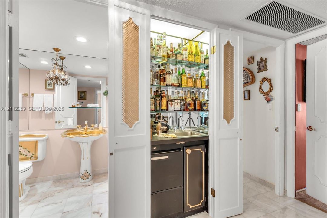 Built-in wet bar featuring glass shelving, mirrored backsplash, and under-counter cabinetry
