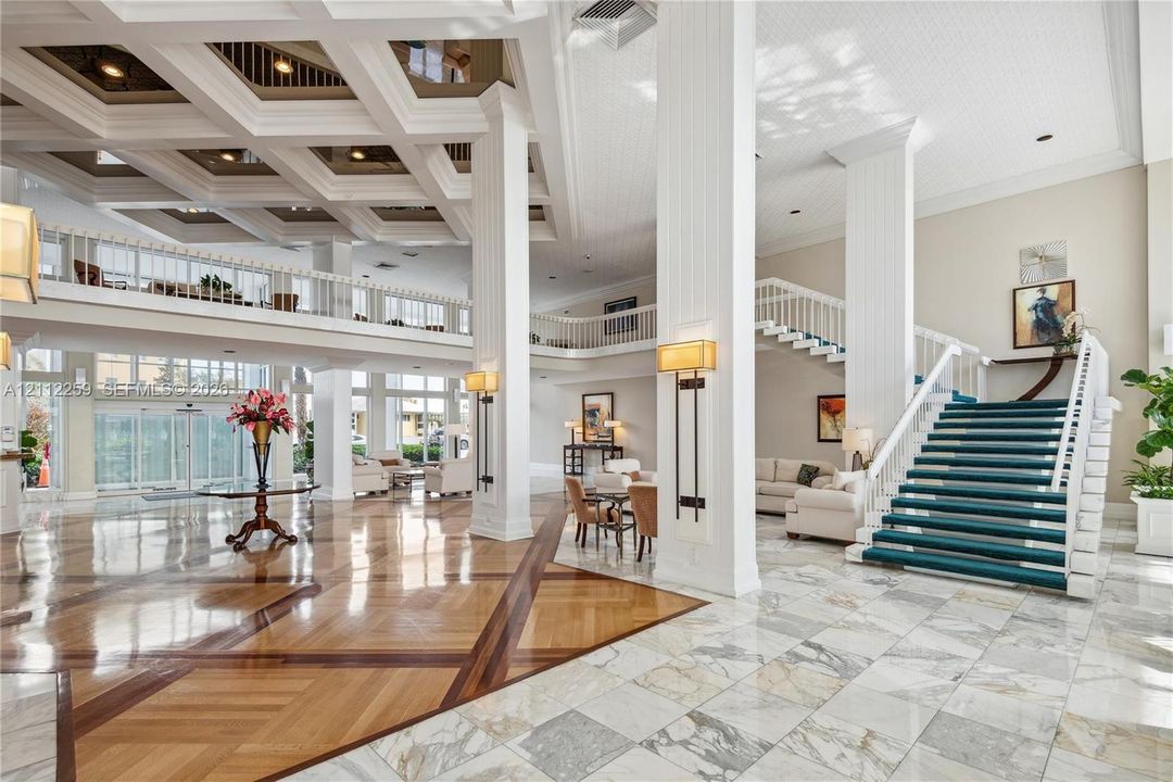 Grand entrance featuring high coffered ceilings, stone-tile flooring with wood-finish inlays, decorative white columns, and a double-railed staircase
