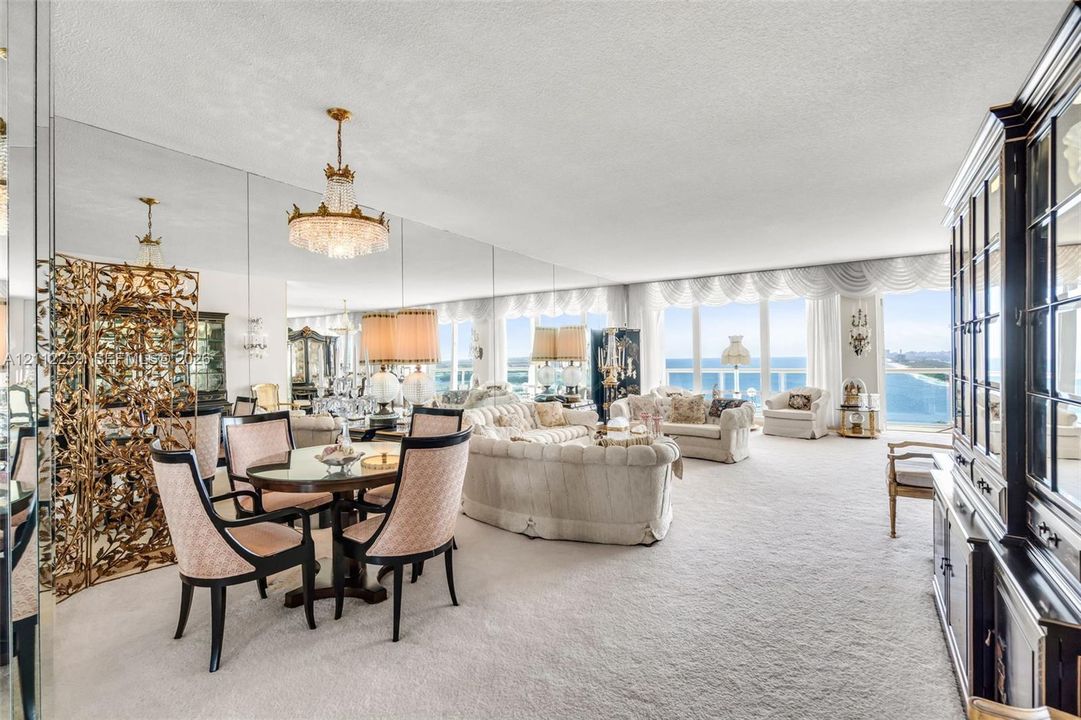 Living area featuring wall-to-wall mirrors, floor-to-ceiling windows with coastal water outlooks, and a crystal chandelier