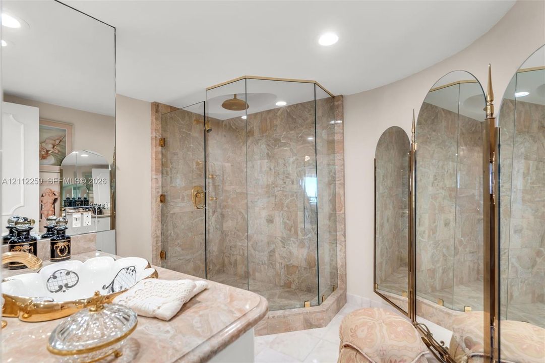 Walk-in corner shower with glass enclosure and stone-tiled surround, stone-topped vanity, and arched wall-mounted mirrors