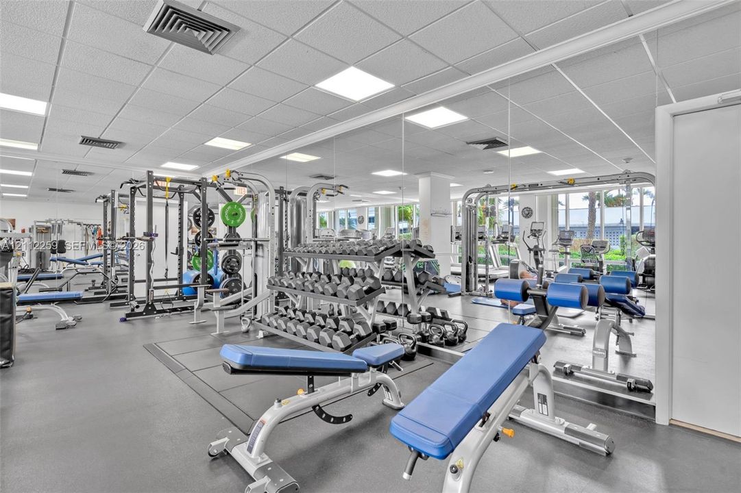 Fitness area featuring a rubberized flooring surface, drop ceiling with recessed panel lighting, and wall-to-wall mirrors
