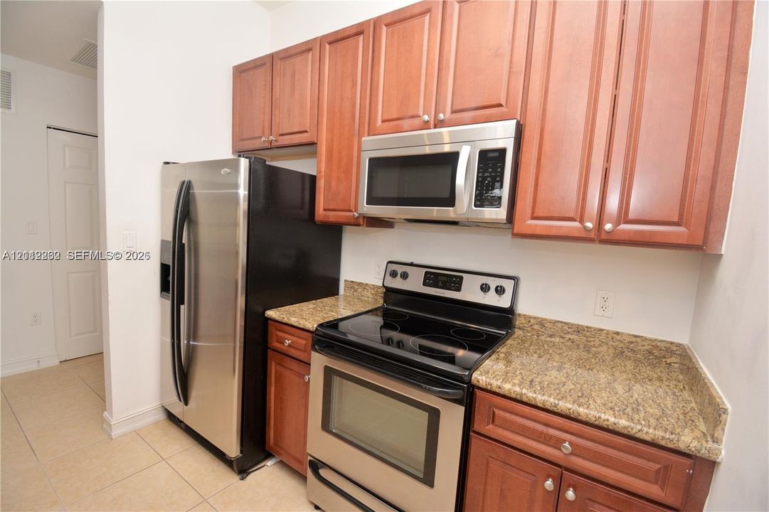 Kitchen featuring wood cabinetry, stone-finish countertops, and a suite of stainless steel appliances, including an over-the-range microwave and a full-size refrigerator