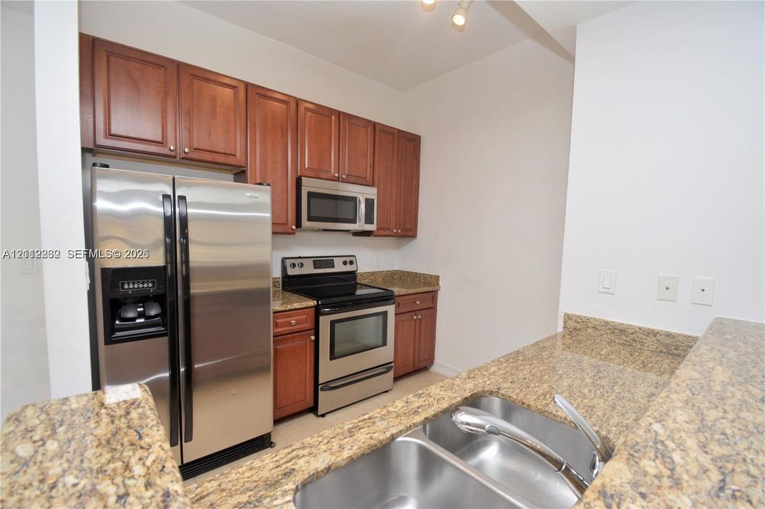 Kitchen featuring wood cabinetry, stone countertops, stainless steel refrigerator, over-the-range microwave, and a dual-basin stainless steel sink