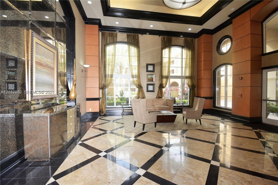 Grand lobby featuring double-height ceilings, arched windows, built-in mirrored wall treatments, coffered ceiling detail, and stone flooring with inlaid geometric patterns