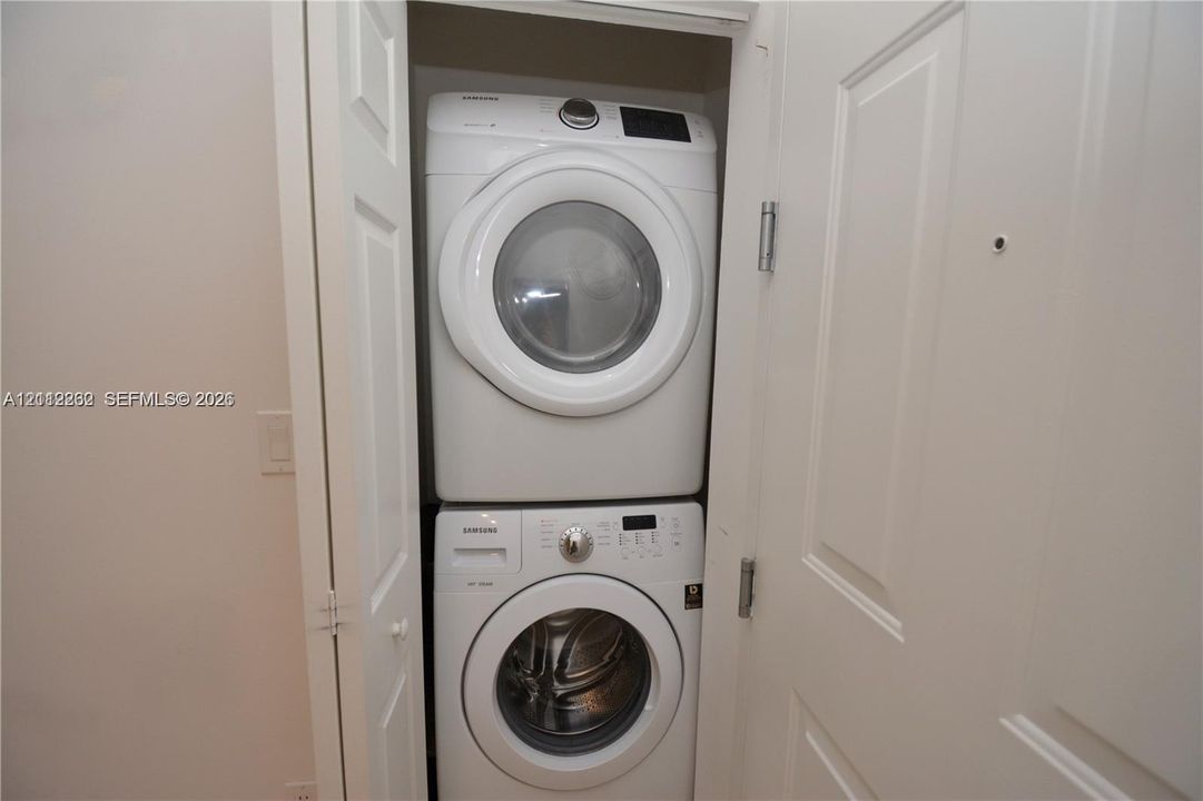 Stacked washer and dryer unit housed in a dedicated closet featuring white bi-fold doors