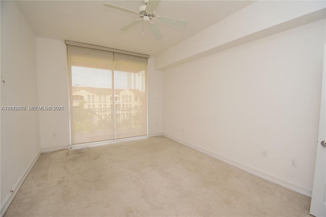 Room featuring neutral carpeting, sliding glass balcony door with roller shade, and a ceiling fan