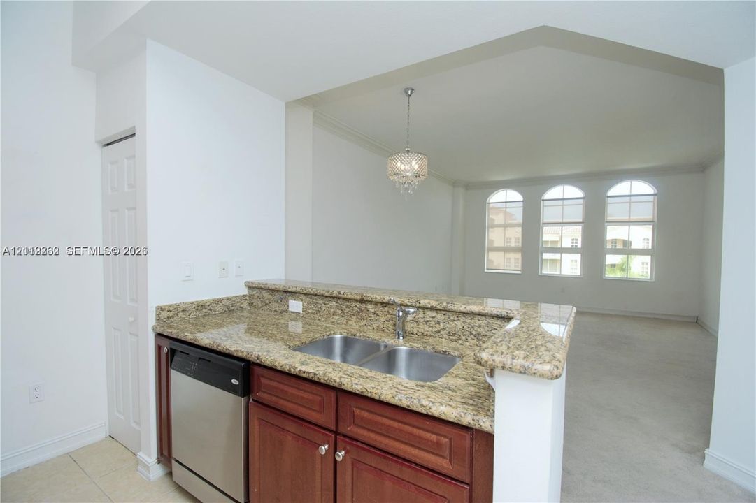 Stone-surfaced peninsula countertop, stainless steel undermount double-basin sink, wood-finish cabinetry, built-in dishwasher, and decorative crystal chandelier