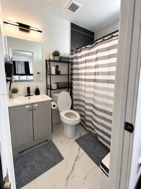 Bathroom featuring a gray vanity with white countertop, integrated sink, matte black faucet, wall-mounted linear vanity light, and large-format white tile flooring with dark veining