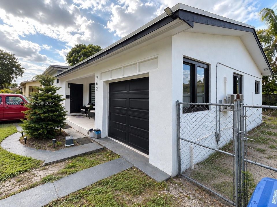 Stucco exterior featuring a covered front porch, integrated single-car garage with dark-toned door, and contrasting dark window frames