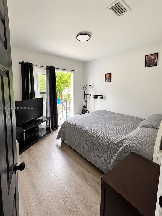 Bedroom featuring wood-finish flooring, flush-mount ceiling lighting, and a glass-paneled sliding door providing exterior access