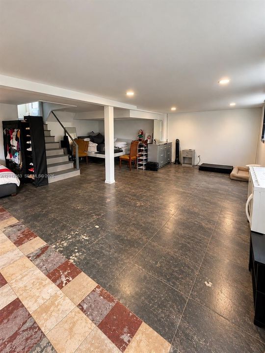 Open-concept interior space featuring large-format dark stone-finish flooring, recessed lighting, and a staircase with a metal handrail and support column