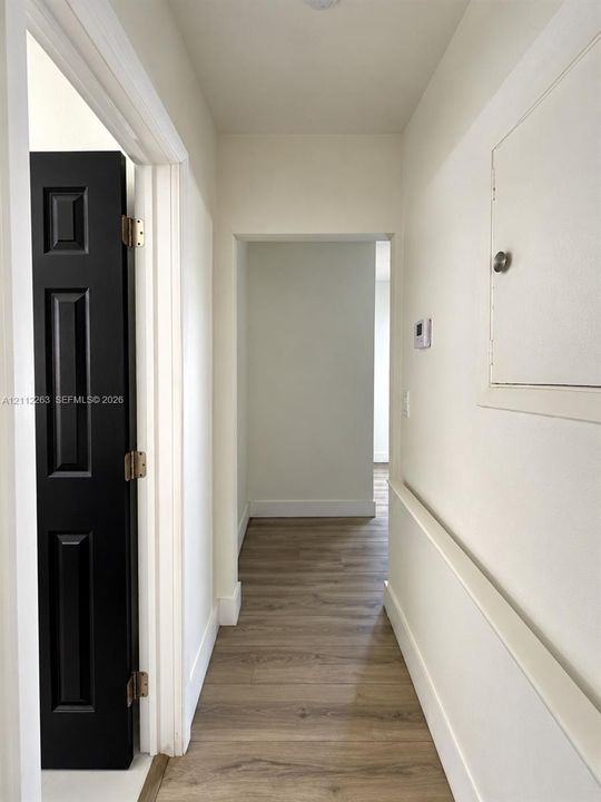Wood-finish flooring, contrast-color interior door with recessed paneling, and wall-mounted access panel