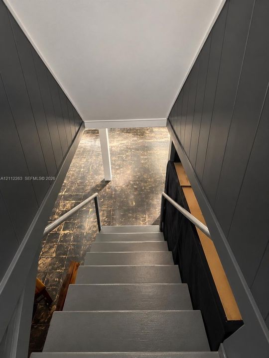 Staircase featuring dark-toned vertical paneled walls, painted treads, and metal handrails