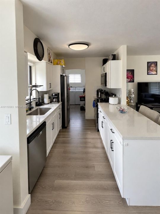 Kitchen featuring white cabinetry with dark hardware, stone-finish countertops, stainless steel undermount sink, wood-finish flooring, and recessed ceiling lighting