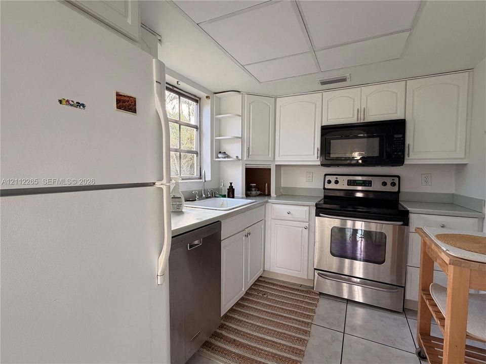 Kitchen featuring white cabinetry with open shelving, stainless steel appliances, solid surface countertops, a white undermount sink, and tiled flooring