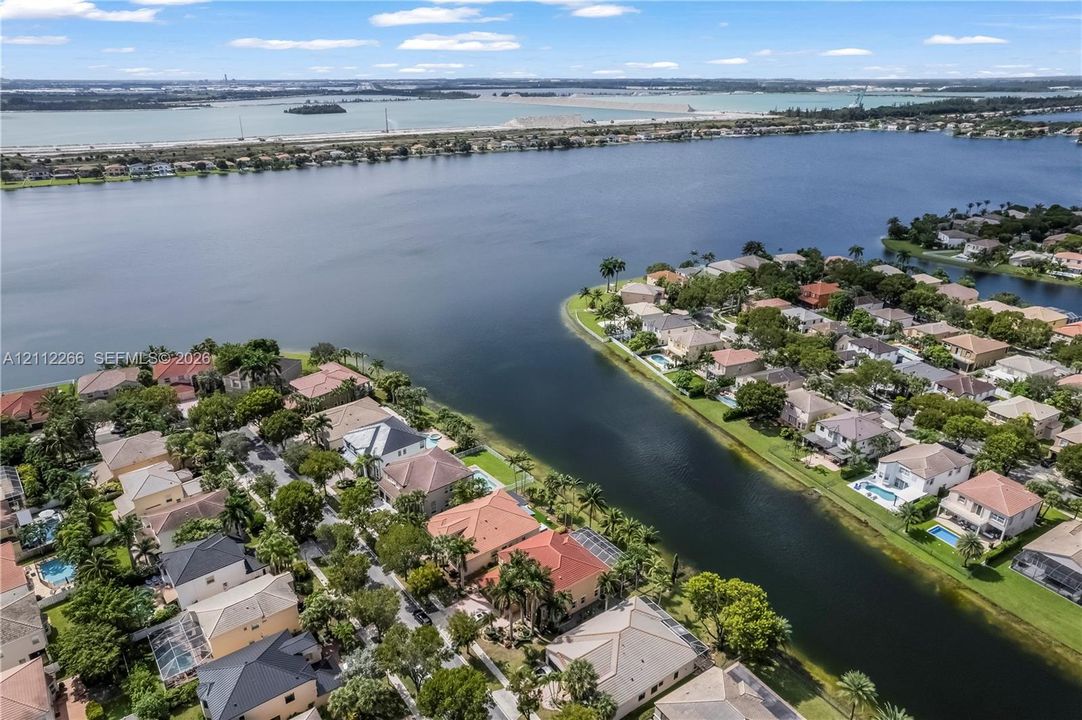 Aerial perspective of waterfront residential community featuring expansive canal frontage, mature trees, and proximity to large-scale coastal water
