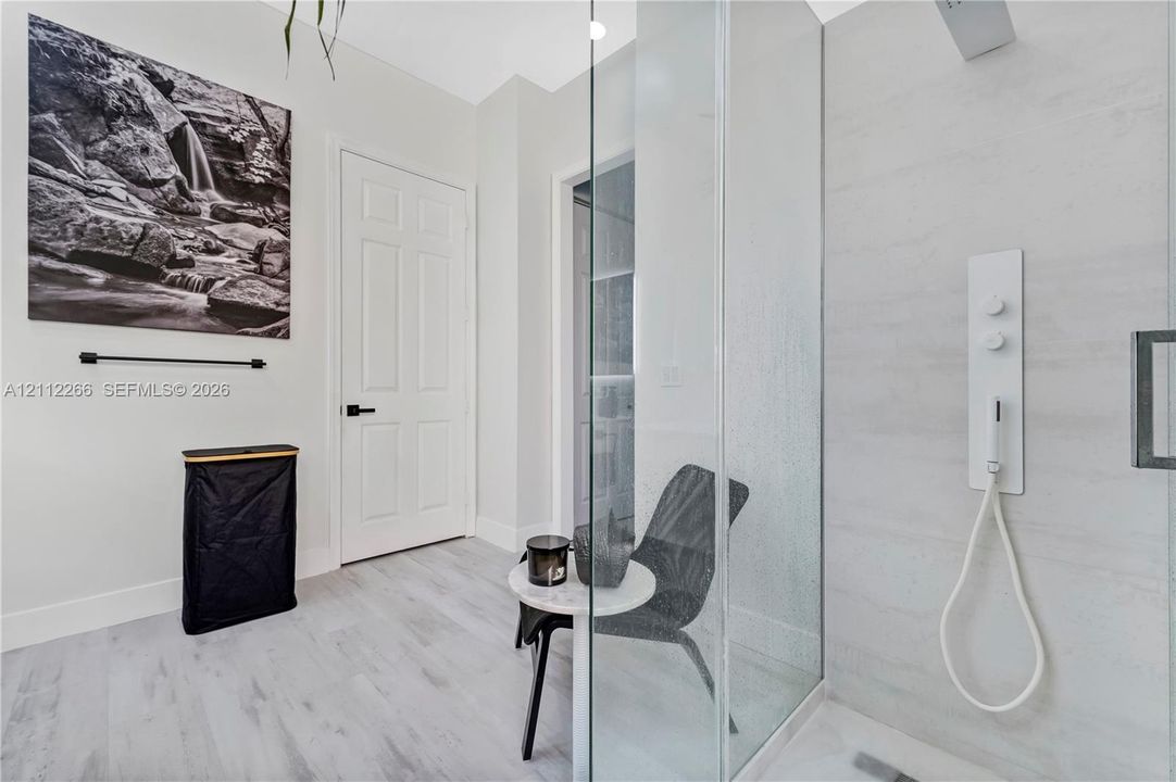 Walk-in shower featuring a glass enclosure, wall-mounted multi-function shower panel, and light-toned wood-finish flooring