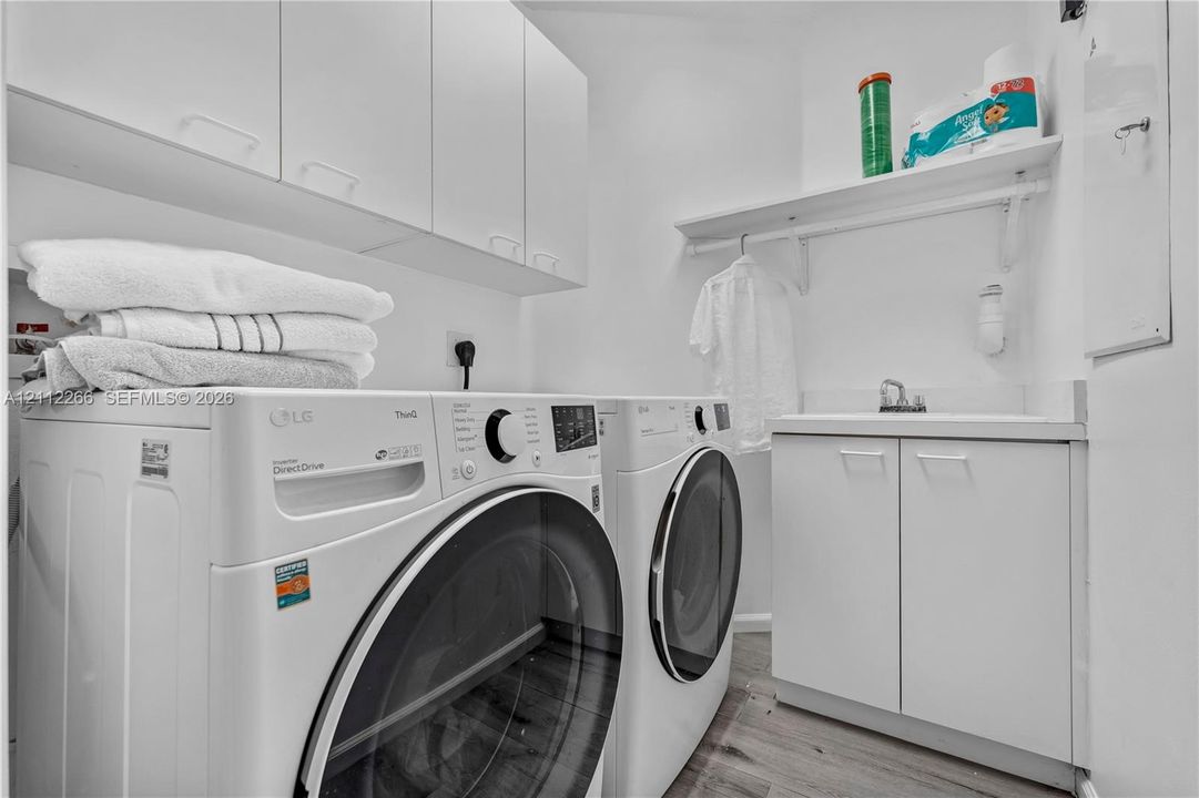 Laundry area featuring white cabinetry, integrated sink, wood-finish flooring, and built-in shelving with a clothes rod
