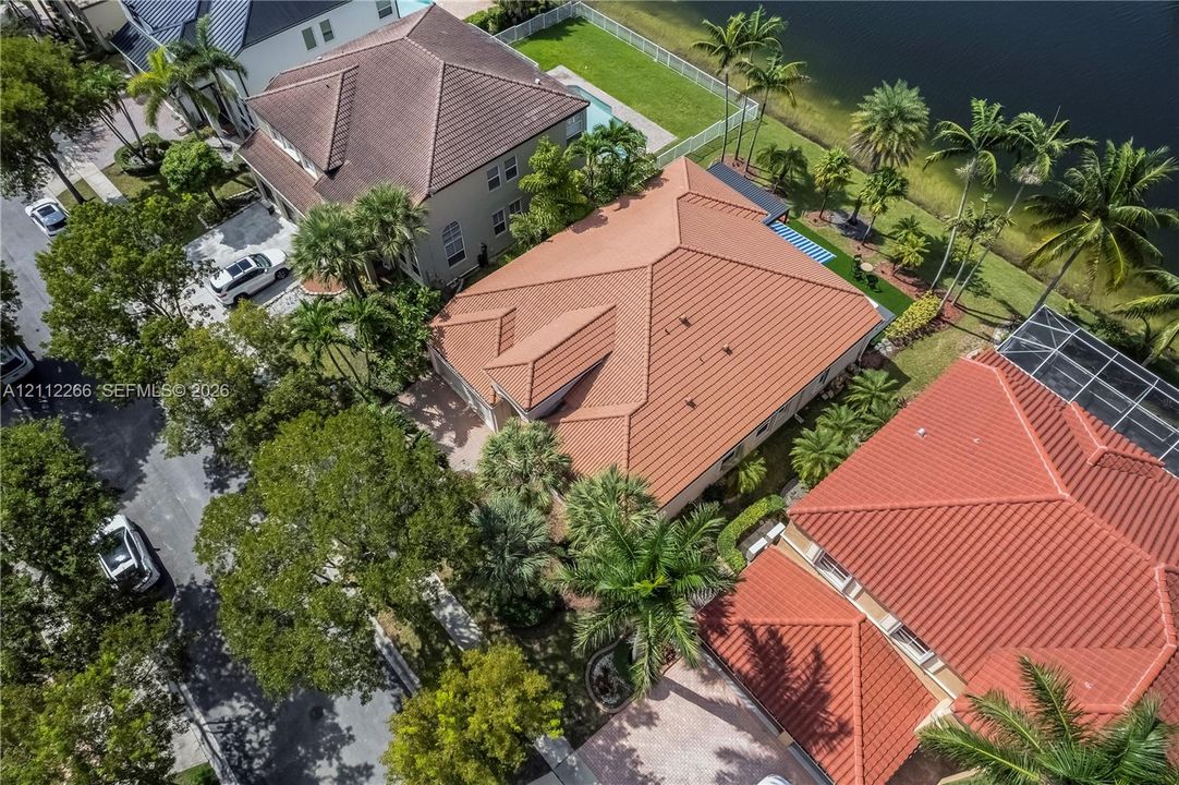 Aerial perspective featuring a tile roof, paved driveway, mature landscaping, and water frontage