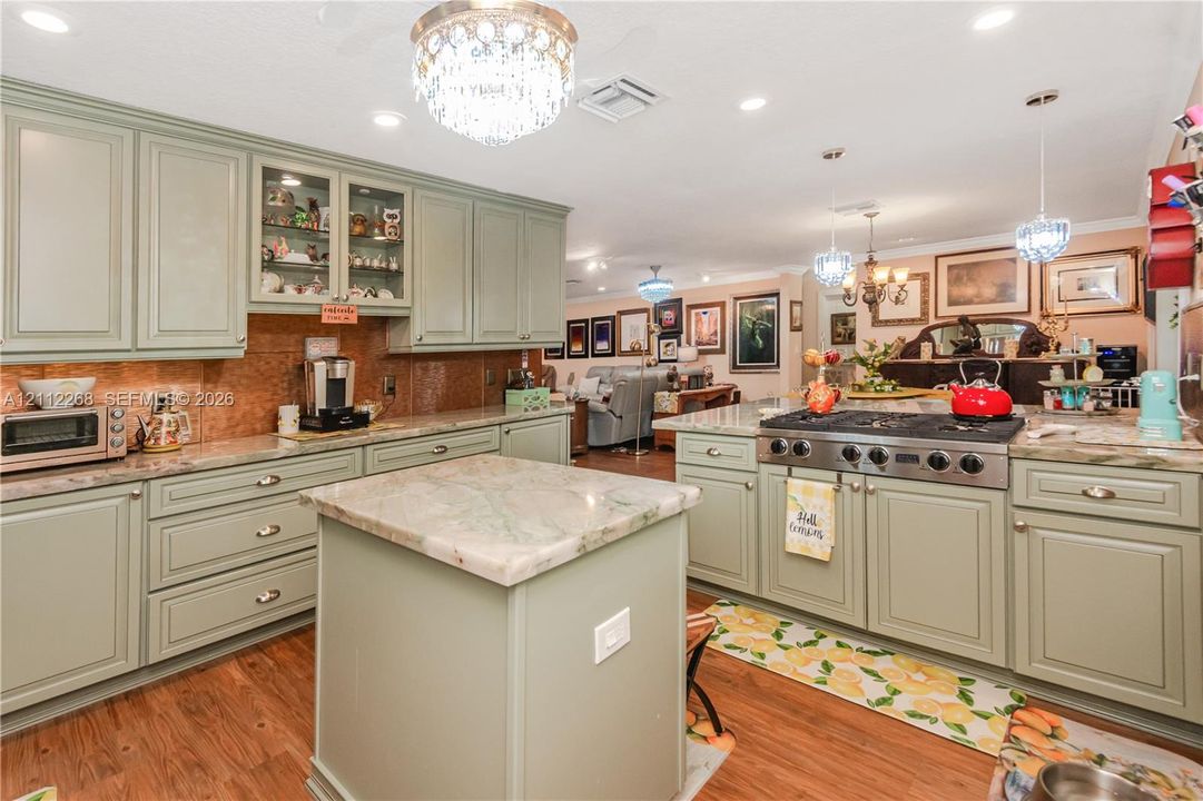 Kitchen featuring custom sage green cabinetry, stone-finish countertops, a central island, recessed lighting, and ornate crystal chandelier fixtures