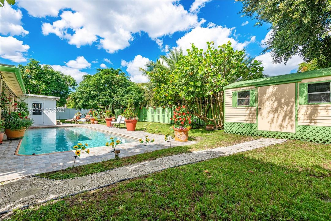 Backyard featuring a concrete-paver patio, swimming pool, detached storage structure, manicured lawn, and perimeter lattice fencing