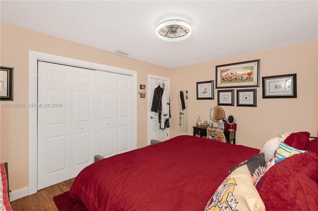 Bedroom featuring wood-finish flooring, a ceiling-mounted light fixture with a decorative rim, and bi-fold closet doors