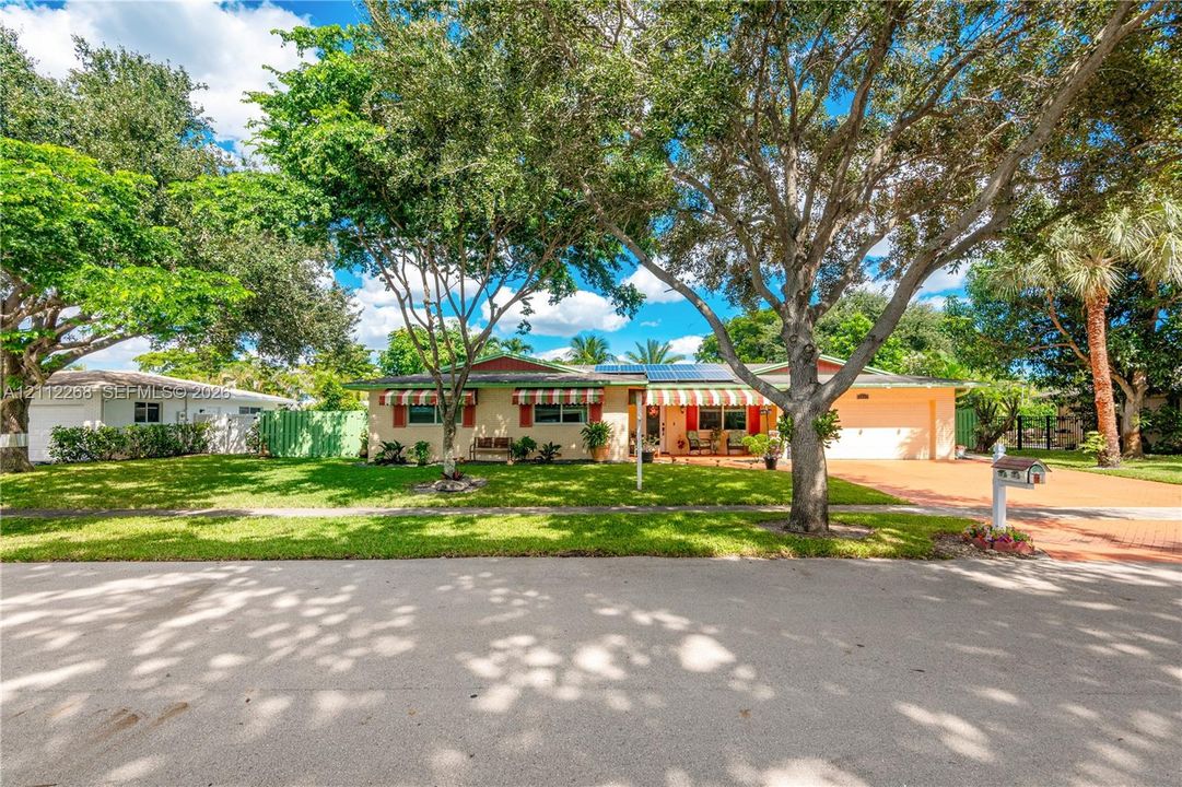 Single-story residence featuring a paved driveway, attached garage, solar panels, and mature landscaping