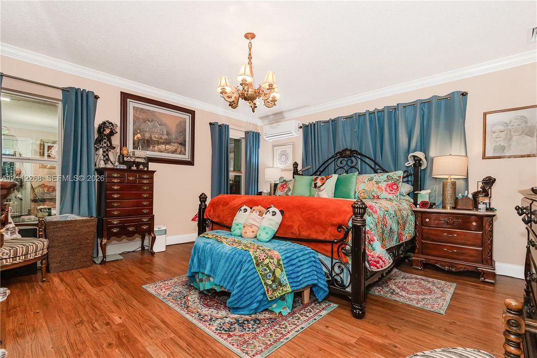 Room featuring wood-finish flooring, crown molding, a wall-mounted ductless mini-split HVAC unit, and a central decorative multi-arm chandelier