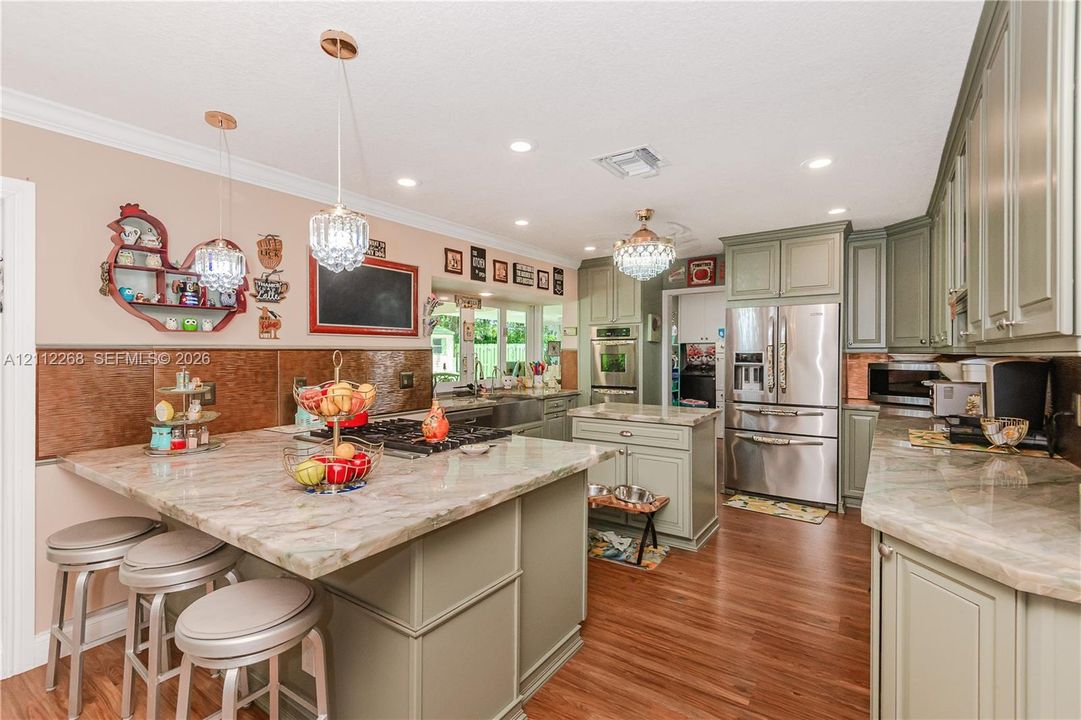 Kitchen featuring sage-toned cabinetry, stone-finish countertops, stainless steel appliances, wood-finish flooring, and multi-light crystal pendant fixtures