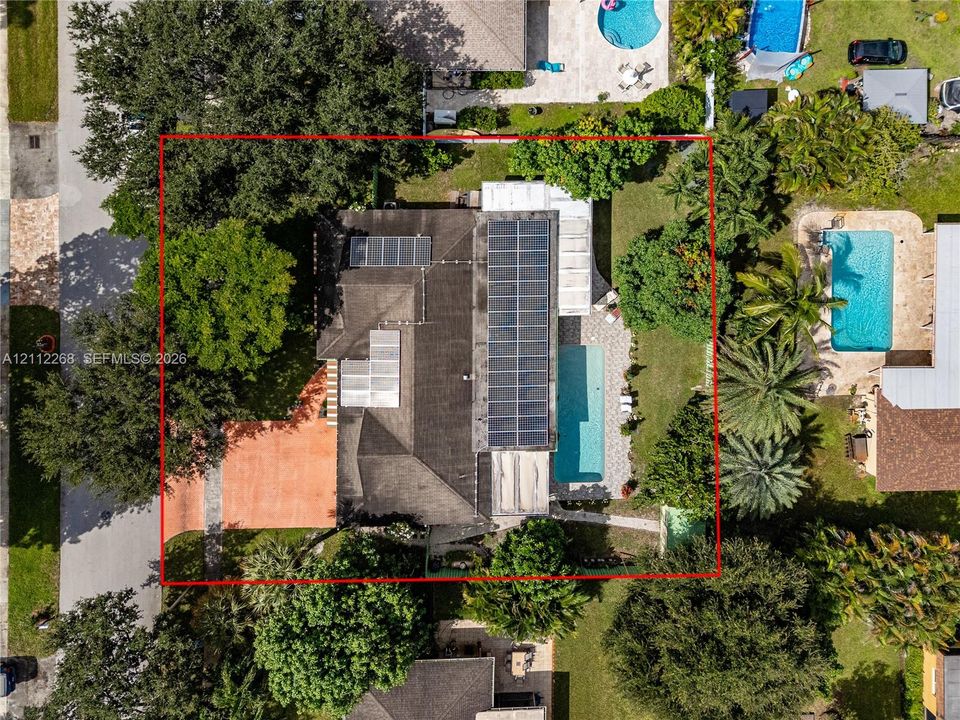 Aerial perspective of a property featuring solar panels, a rectangular swimming pool, a paved patio area, and mature landscaping