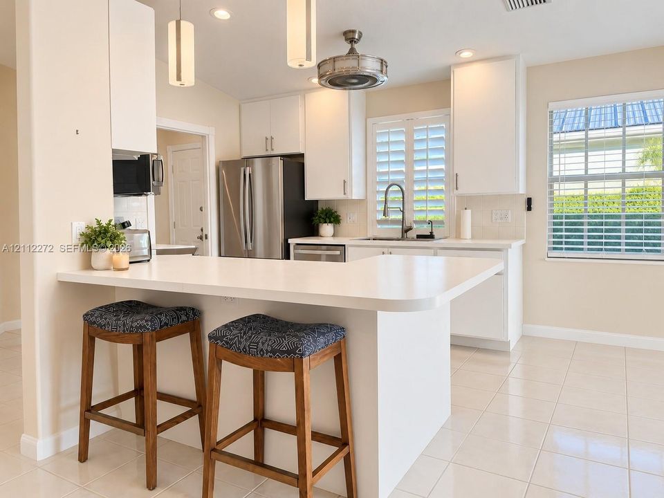 Kitchen featuring white cabinetry, solid-surface countertops with an integrated breakfast bar, stainless steel appliances, tile flooring, and interior window shutters
