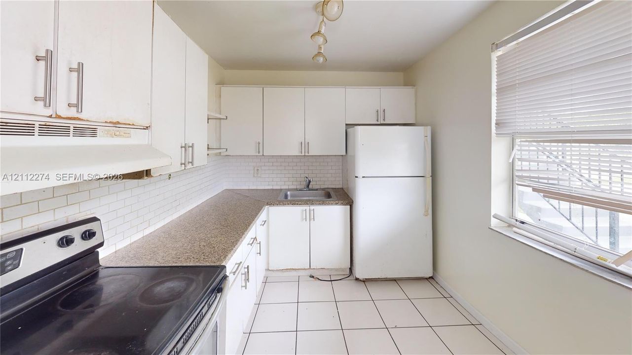 Kitchen featuring white cabinetry, solid surface countertops, a white tile backsplash, ceramic tile flooring, and integrated white appliances
