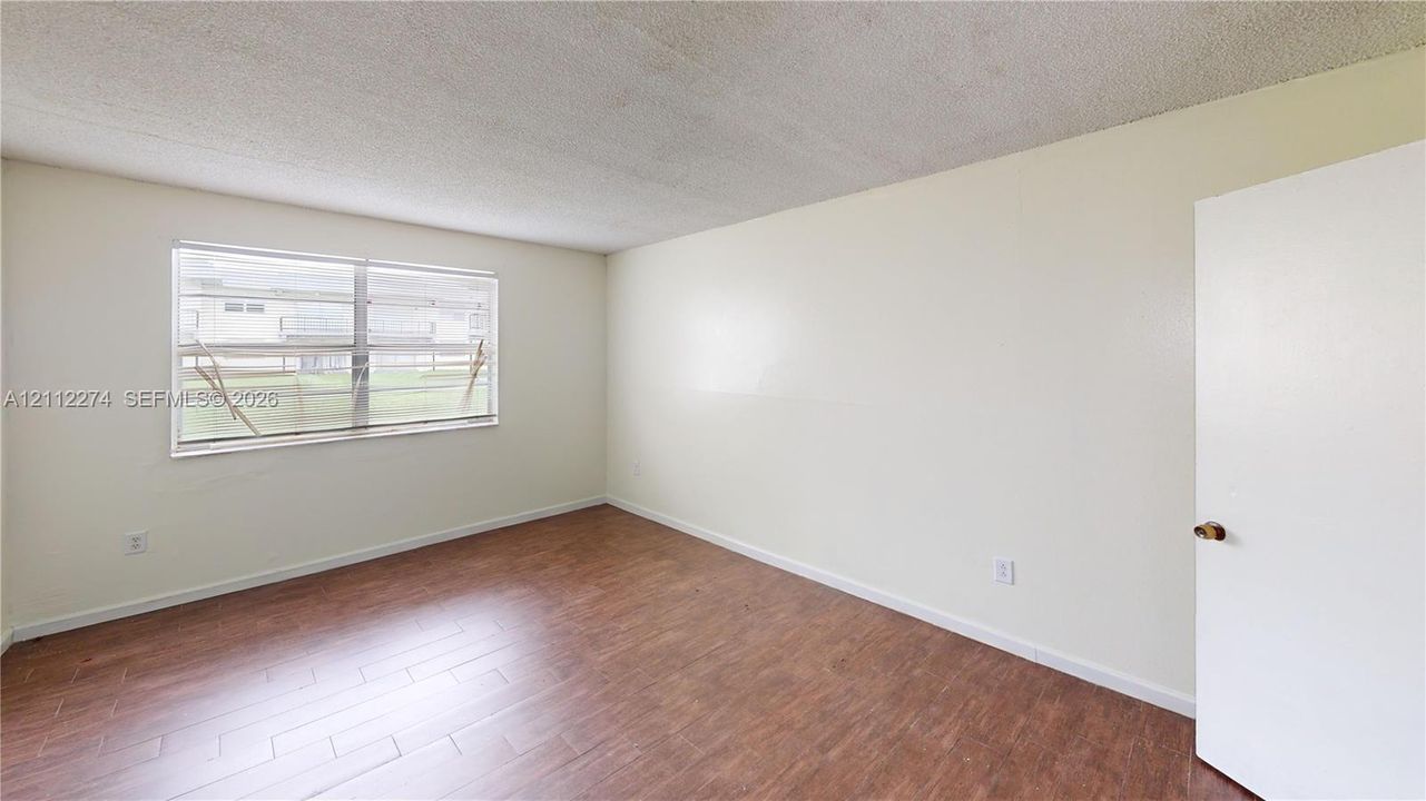 Room interior featuring wood-finish flooring, neutral wall paint, and a single-pane horizontal window