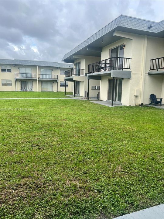 Exterior facade featuring stucco siding, elevated balconies with metal railings, sliding glass doors, and expansive grassy grounds