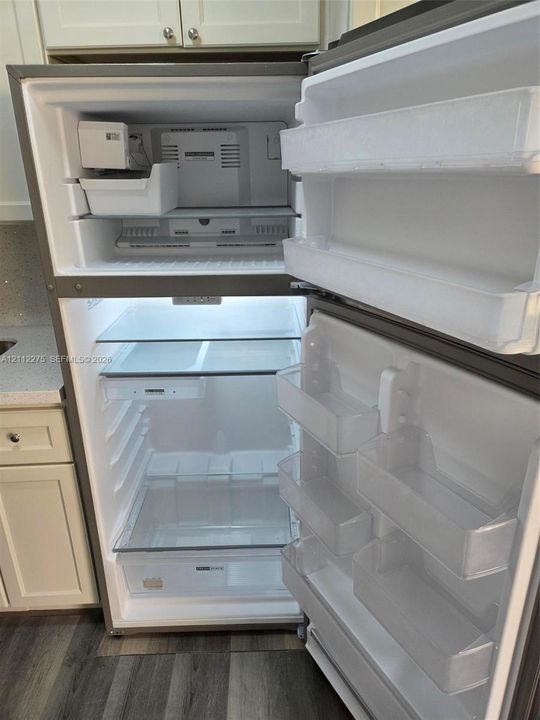 Stainless steel top-freezer refrigerator featuring an integrated ice maker, adjustable glass shelving, clear produce drawers, and interior LED lighting