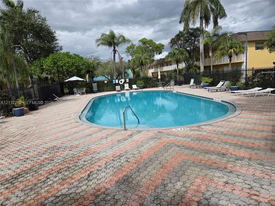Oval swimming pool featuring a metal entry rail, surrounded by patterned paver hardscaping and perimeter fencing