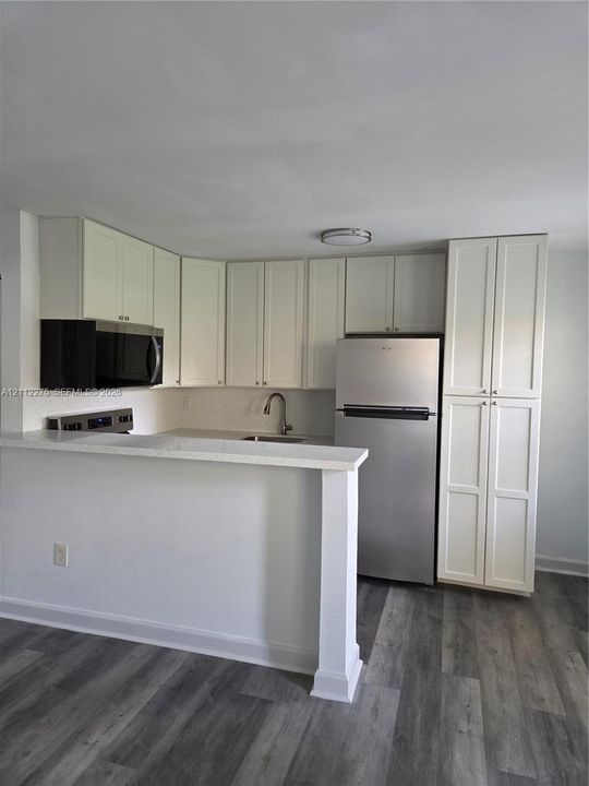 Kitchen featuring white shaker-style cabinetry, a stone-finish countertop with an integrated breakfast bar, stainless steel appliances, and wood-finish flooring