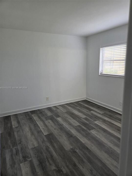 Neutral interior featuring wood-finish flooring and a window with horizontal blinds