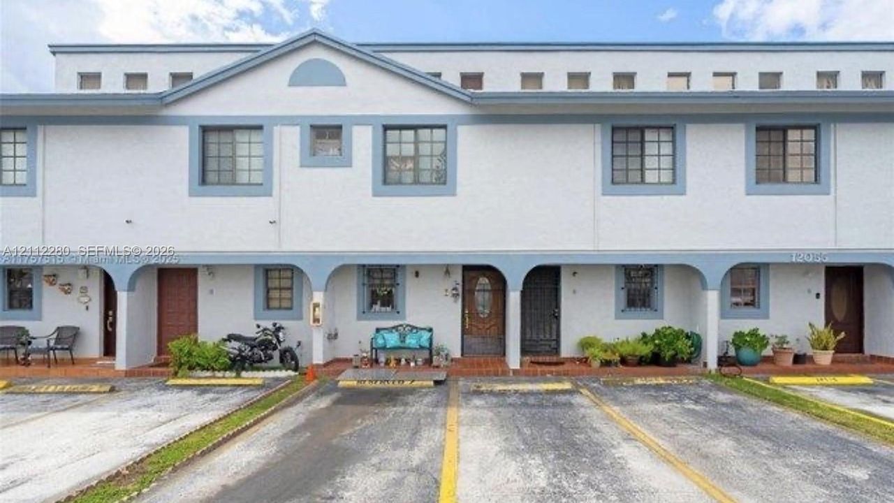 Two-story facade featuring textured stucco exterior, decorative archways, upper-level square transom windows, and dedicated ground-level parking spaces