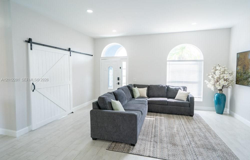 White sliding barn door, arch-top windows, light-tone tile flooring, and recessed ceiling lighting