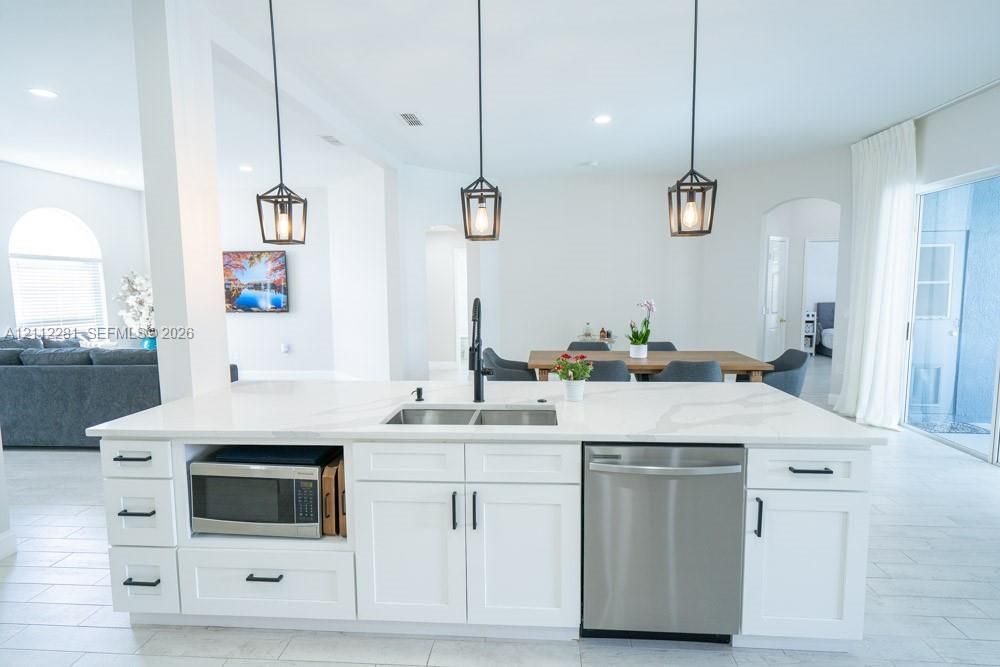 Kitchen island featuring stone-look countertops, white shaker-style cabinetry, matte black hardware, three geometric pendant lights, and a stainless steel undermount sink with a high-arch faucet