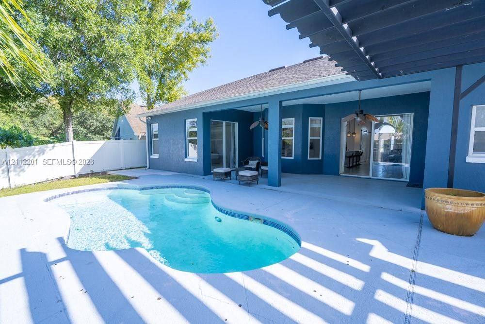 Covered rear patio featuring a pergola, concrete decking, and an inground swimming pool with integrated steps, enclosed by privacy fencing