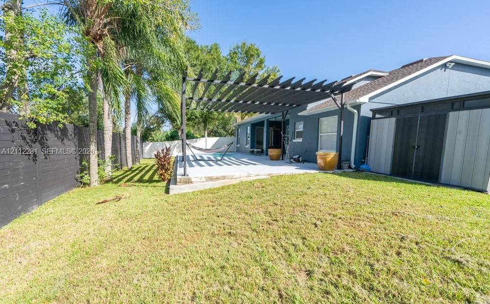 Backyard featuring a concrete patio, black metal pergola, horizontal slat fencing, and mature palm trees