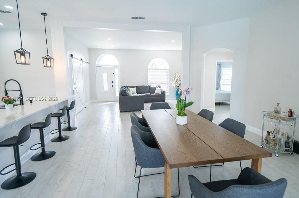Open-concept interior featuring wood-finish flooring, breakfast bar with pendant lighting, arched windows, and a sliding barn-style door