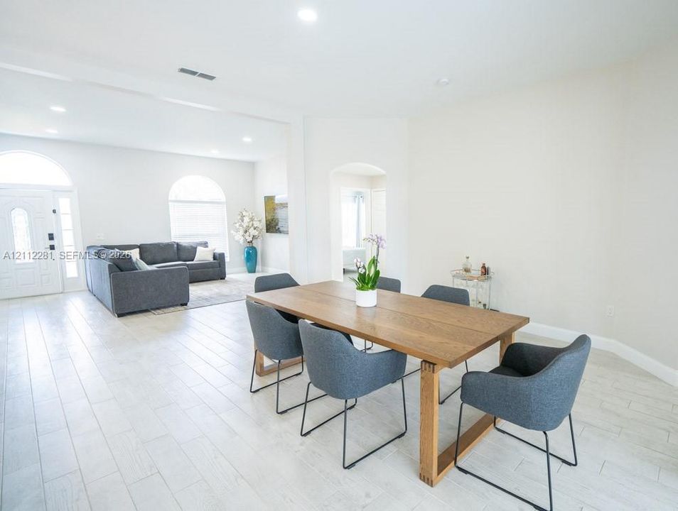 Open-concept interior featuring wood-finish tile flooring, arched windows, recessed lighting, and a prominent arched entryway