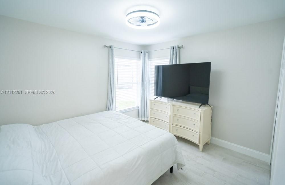 Neutral interior room featuring light-toned wood-finish flooring, dual windows with wall-mounted curtain rods, and a circular LED flush-mount ceiling light